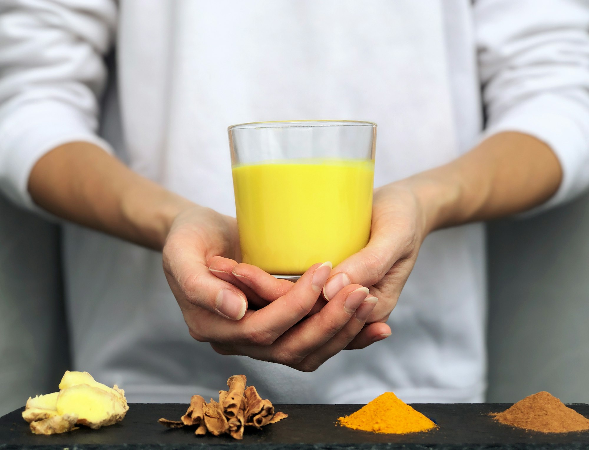 Hands holding a glass of golden milk (turmeric milk) - alternative medicine concept, naturopathy